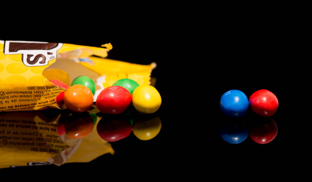 Разноцветные конфеты  M&m's отражаются в черной поверхности стола 