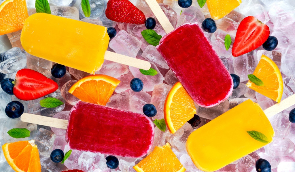 Разноцветное фруктовое мороженое с ягодами лежит на кусочках льда