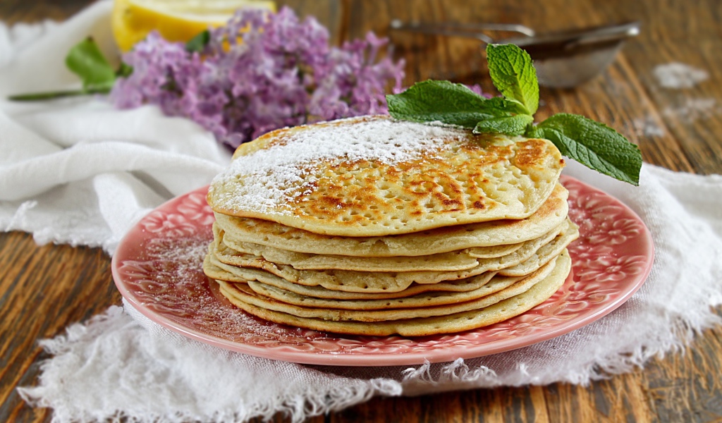 Тонкие блинчики на тарелке с сахарной пудрой и веточкой мяты