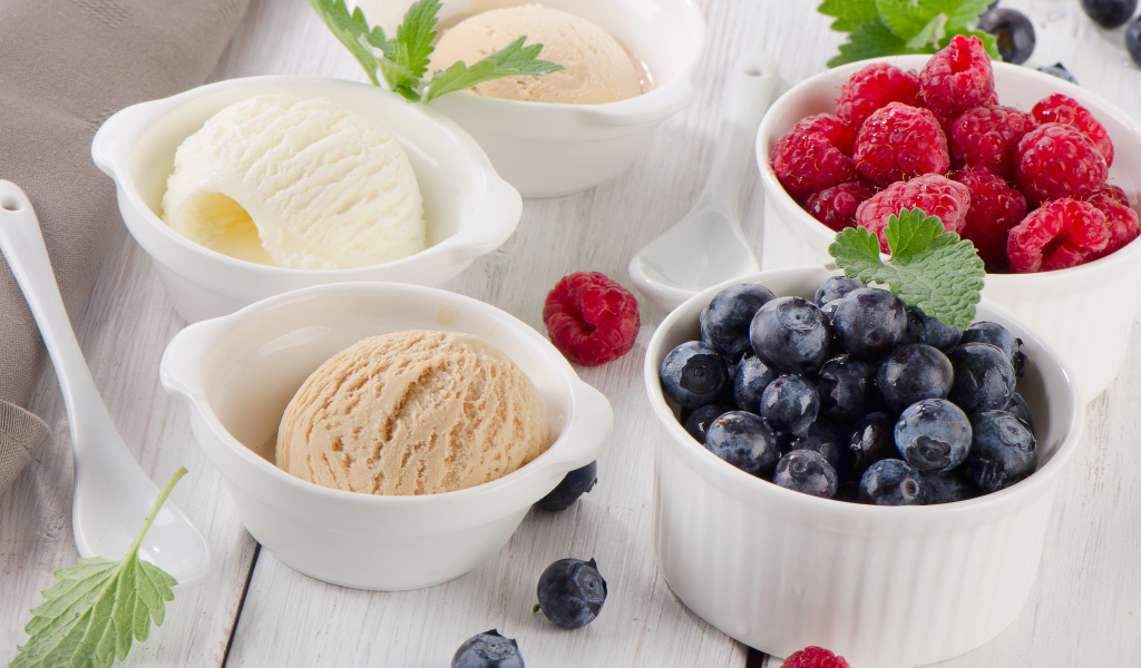 Три шарика мороженого и свежие ягоды малины и черники в белых тарелках
