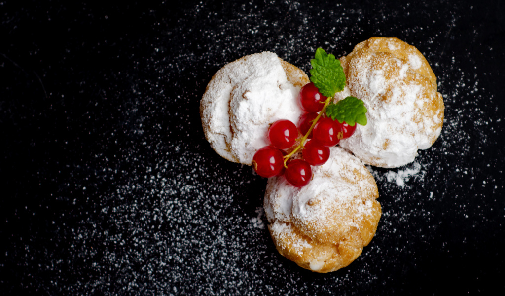 Три пирожных с сахарной пудрой и красной смородиной на черном фоне