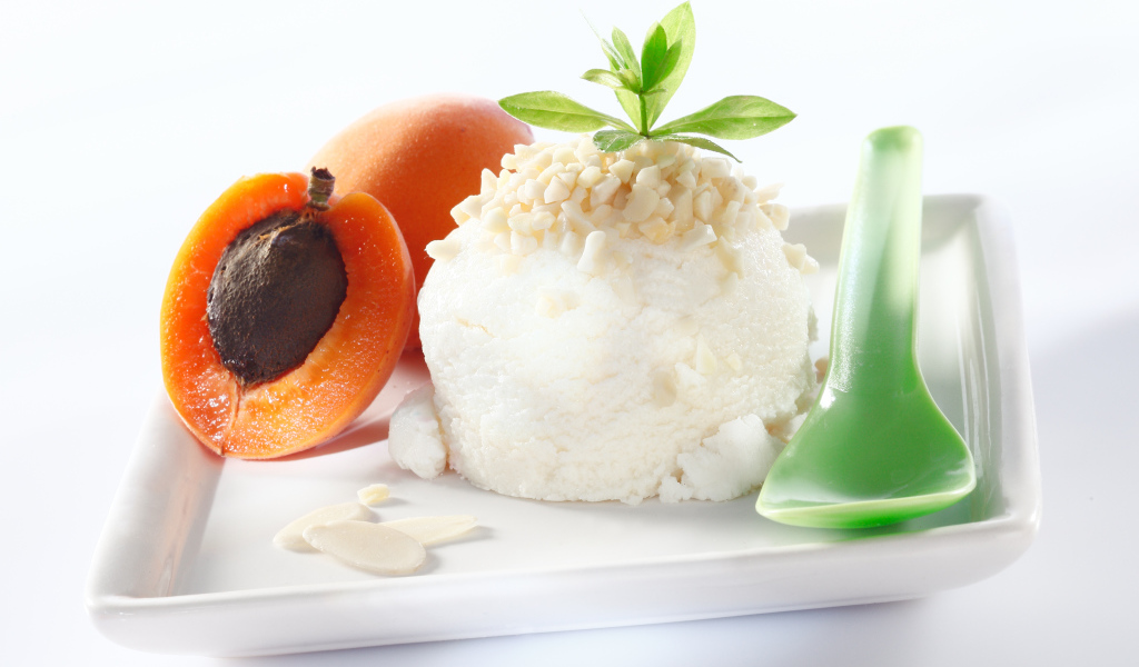 Шарик ванильного мороженого с абрикосами на белой тарелке с ложкой