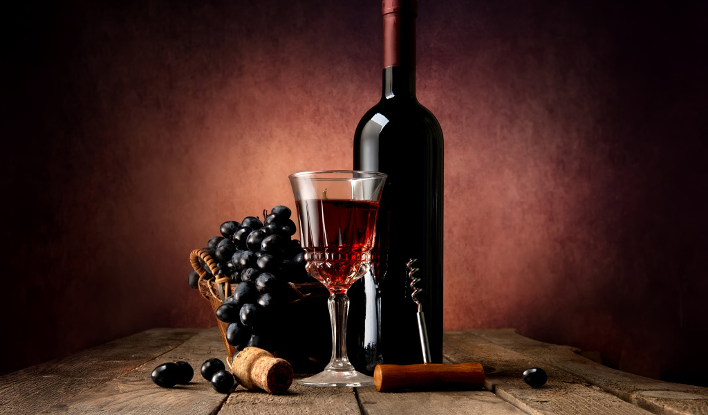 Бутылка красного вина на столе с бокалом и синим виноградом