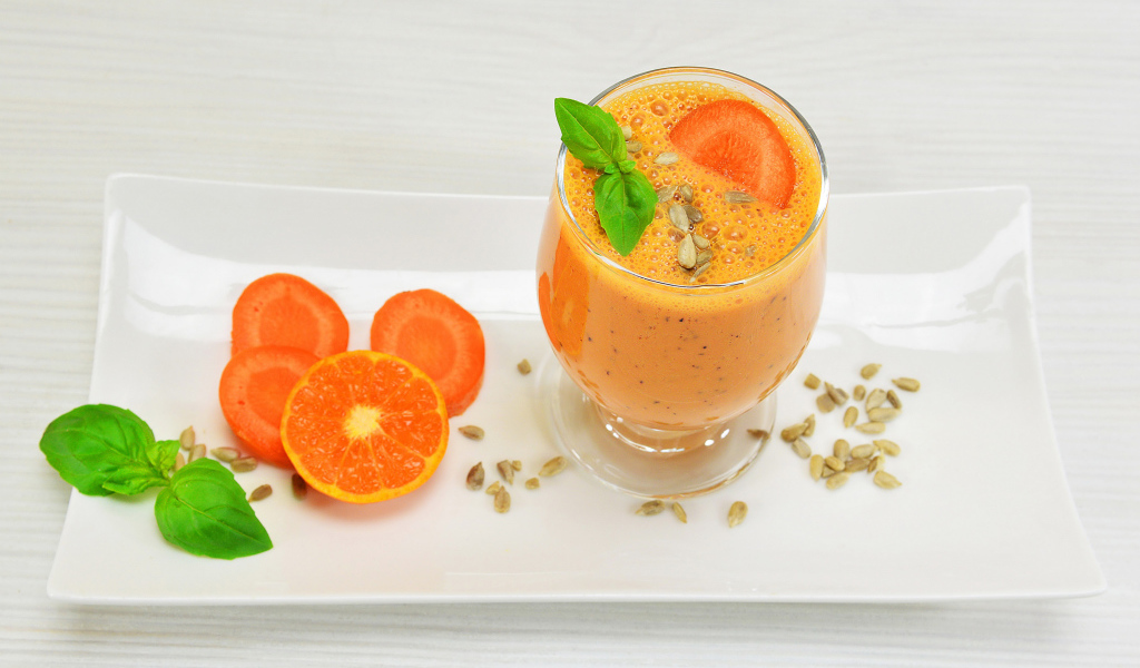 Бокал морковного коктейля с апельсином на белой тарелке
