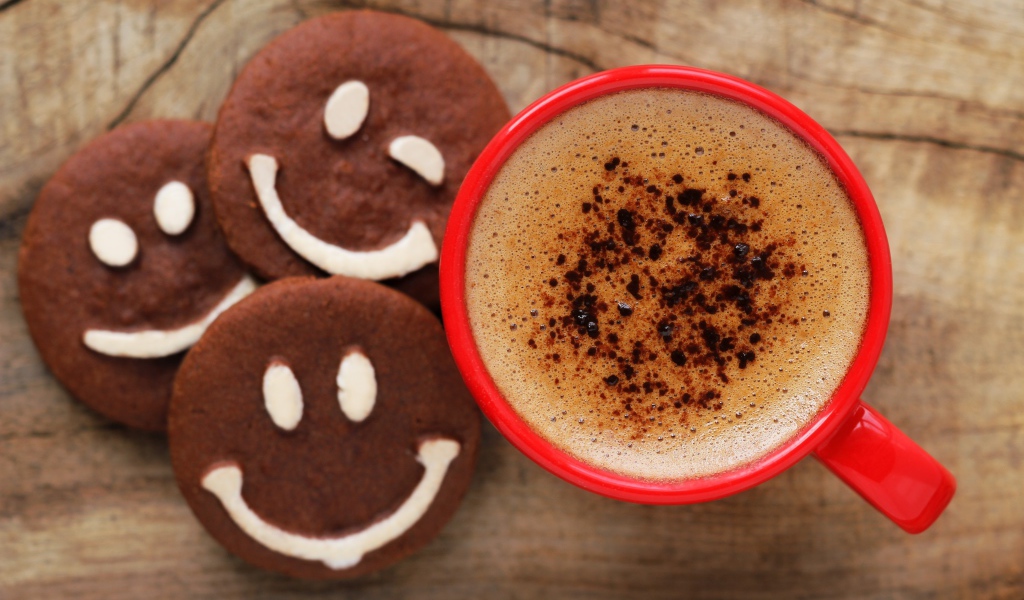 Красная чашка кофе с печеньем смайлами на столе