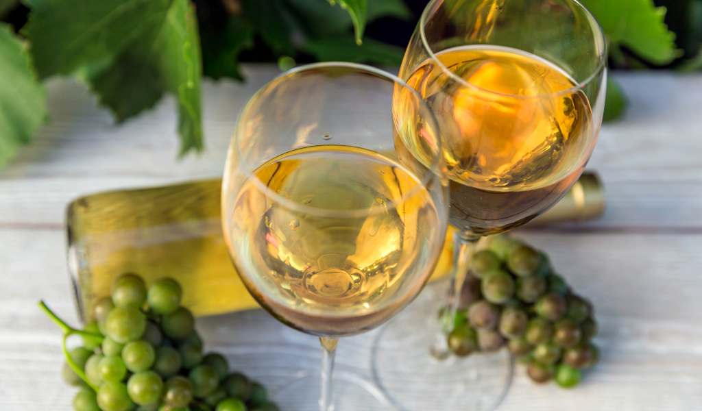 Два бокала белого вина с белым виноградом на столе