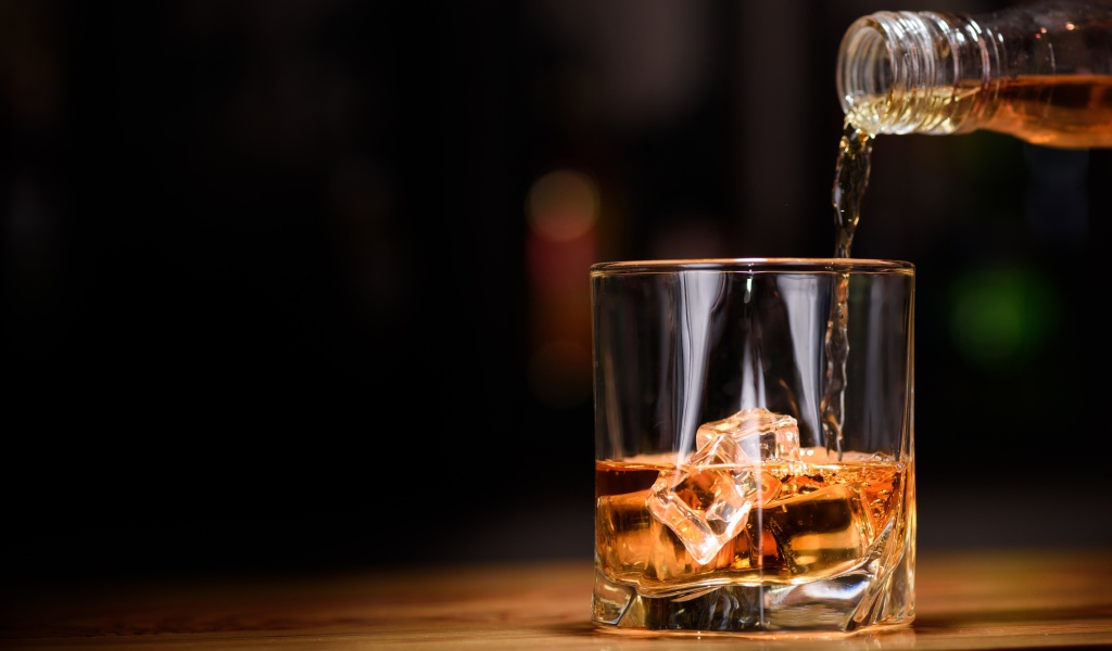 Виски наливают из бутылки в стакан со льдом
