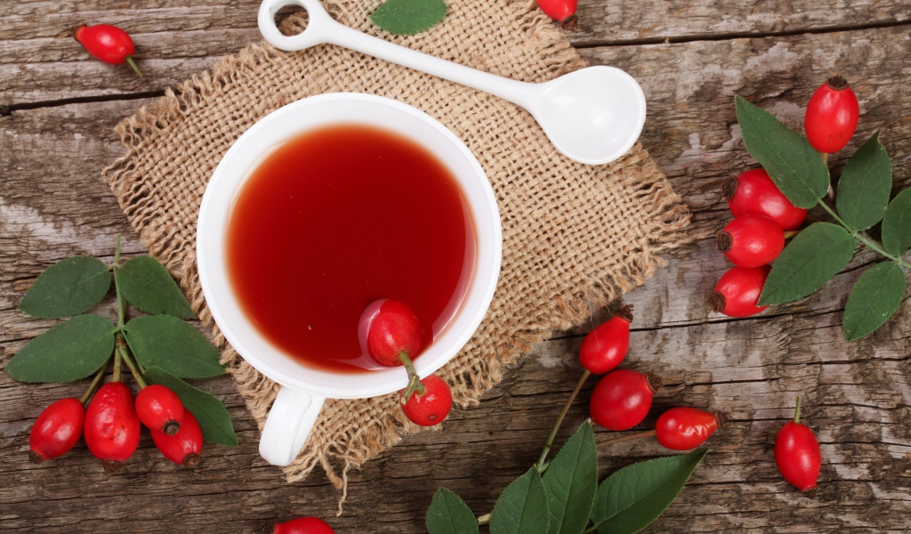 Белая чашка чая с ягодами шиповника на столе
