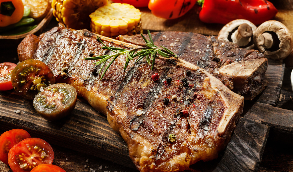 Кусок сочного жареного мяса на разделочной доске с овощами