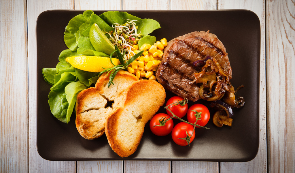 Аппетитный кусок жареного мяса на тарелке с овощами и гренками