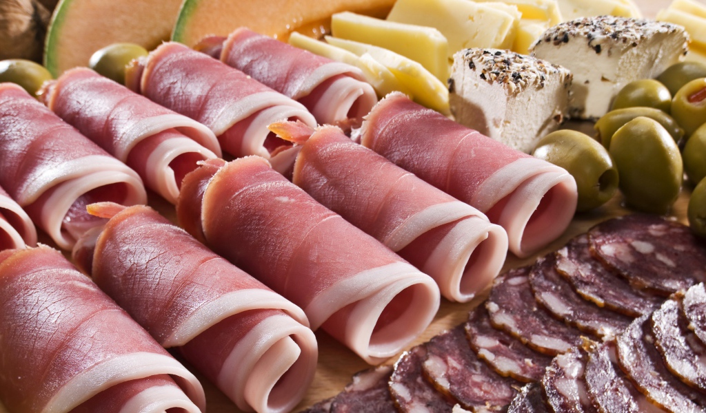 Аппетитные рулетики из бекона на тарелке с зелеными оливками