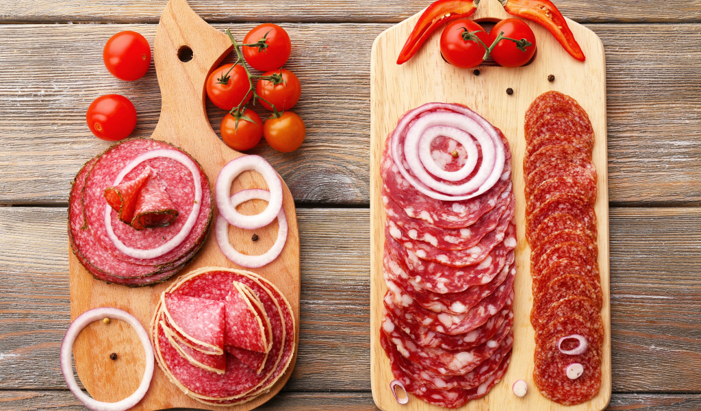 Аппетитная колбасная нарезка на разделочной доске с кольцами лука