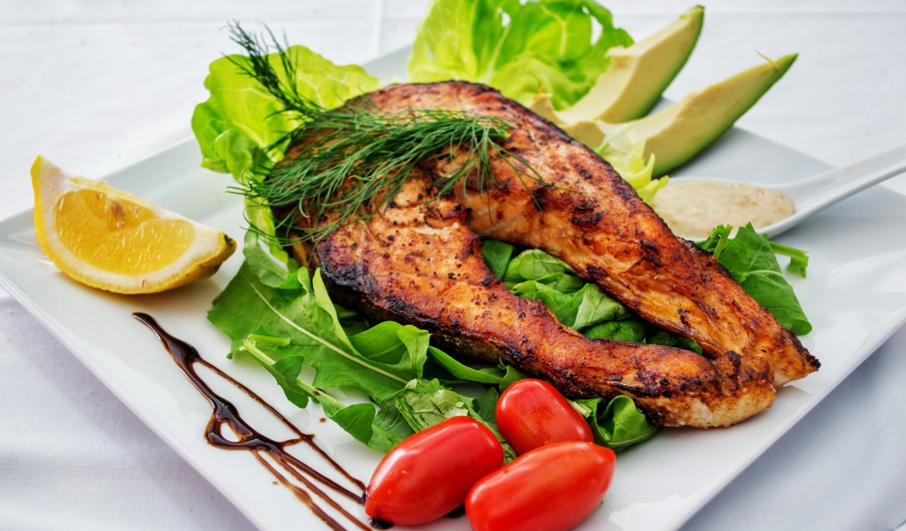 Кусок жареной рыбы на белой тарелке с овощами