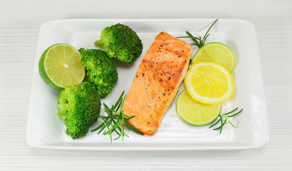 Красная рыба на белой тарелке с лимонами и брокколи