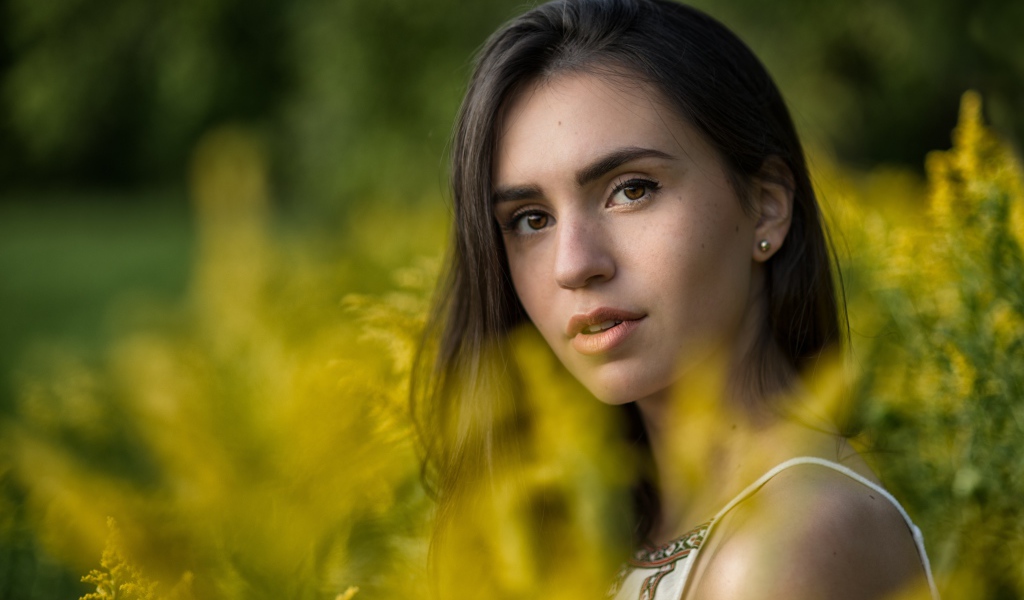 Красивая девушка с нежным взглядом сидит у желтых цветов
