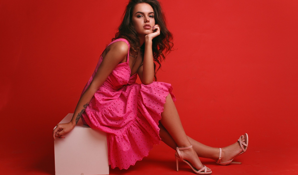 Девушка сидит на белом кубе, фото на красном фоне 