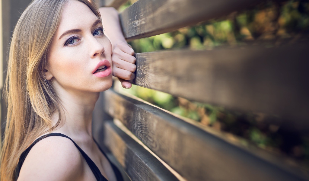 Красивая голубоглазая девушка у деревянного забора 