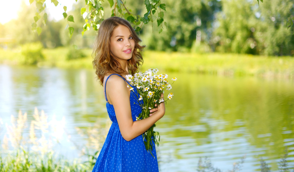 Красивая девушка шатенка в синем сарафане с букетом ромашек у воды