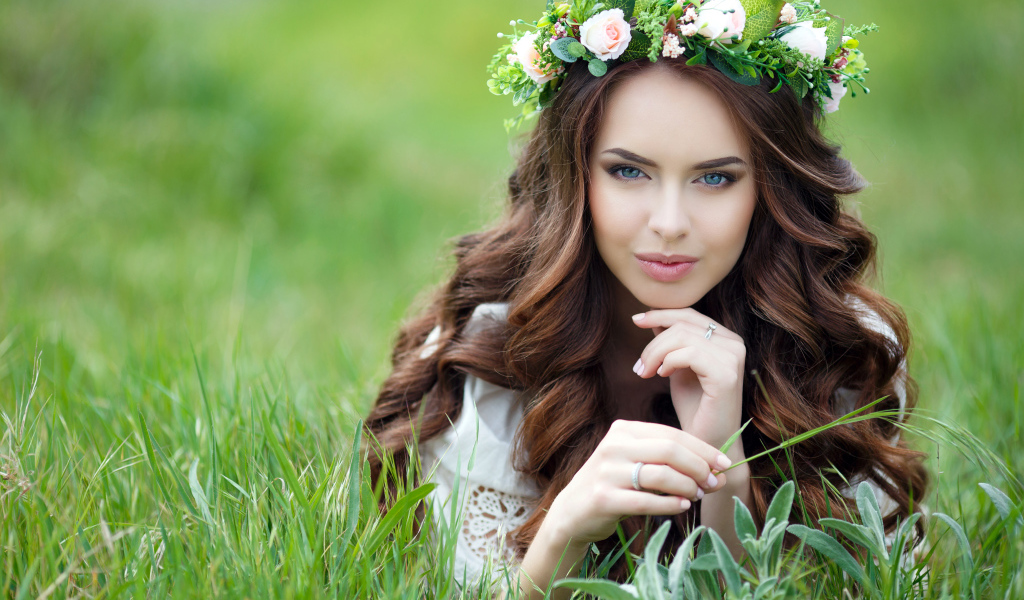 Красивая девушка шатенка с венком на голове лежит на зеленой траве