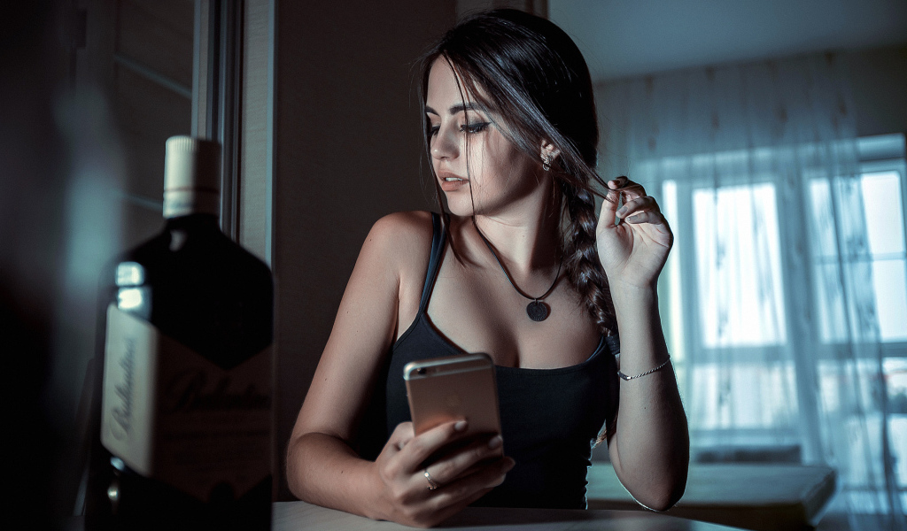 Красивая брюнетка с телефоном в руках и бутылкой
