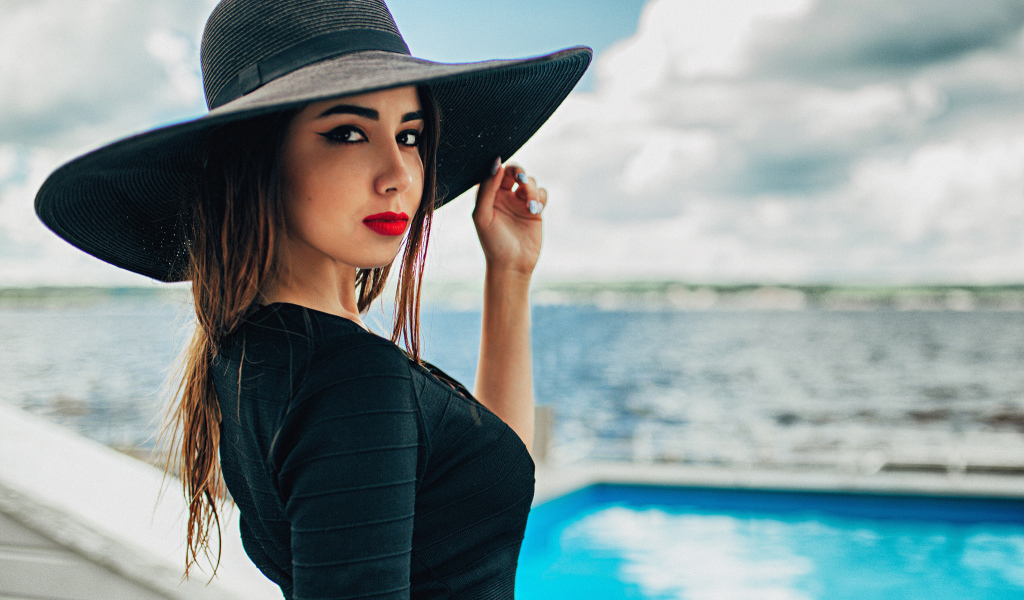 Красивая девушка в большой черной шляпе у бассейна