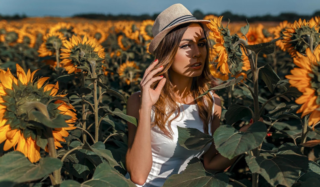 Красивая девушка в шляпе стоит на поле с подсолнухами