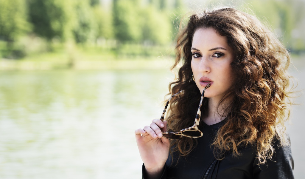 Красивая девушка с волнистыми волосами с очками в руках 