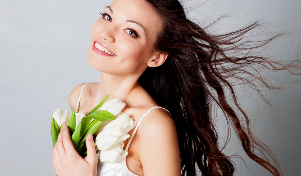 Красивая улыбающаяся брюнетка с букетом тюльпанов на сером фоне