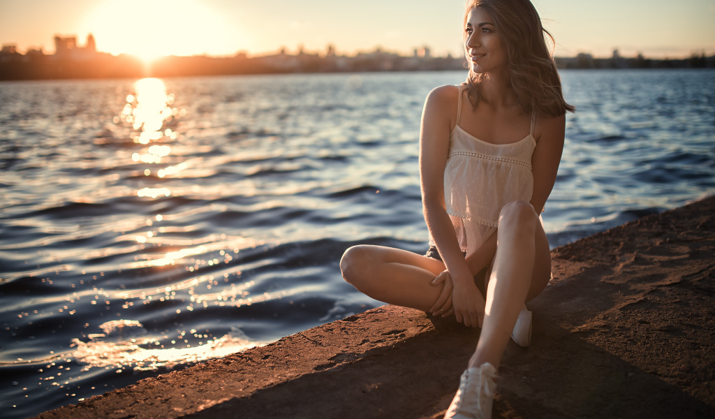 Красивая улыбающаяся девушка сидит в лучах солнца у реки