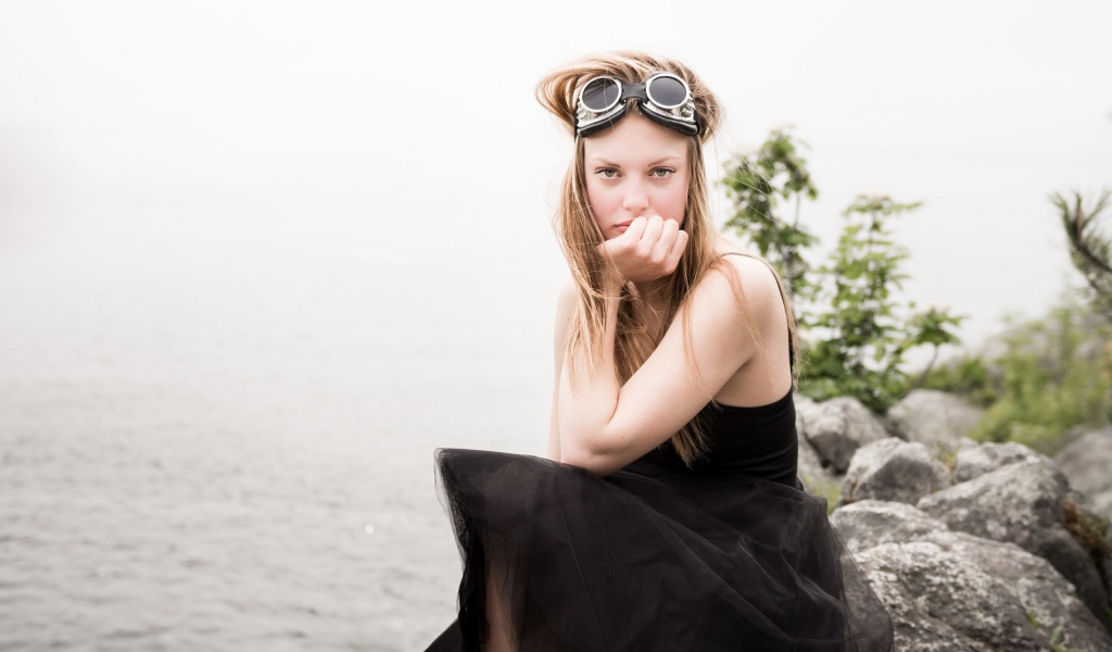 Девушка блондинка с очками на голове сидит на камне