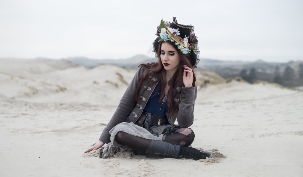 Девушка брюнетка  в костюме сидит на песке 