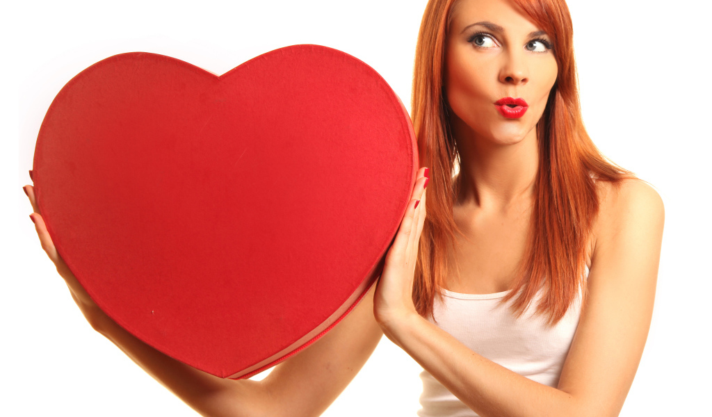 Рыжеволосая девушка с большим красным сердцем в руках на белом фоне