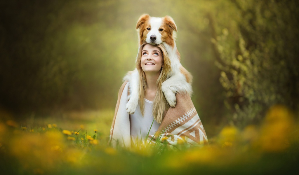 Улыбающаяся девушка с собакой сидят на траве