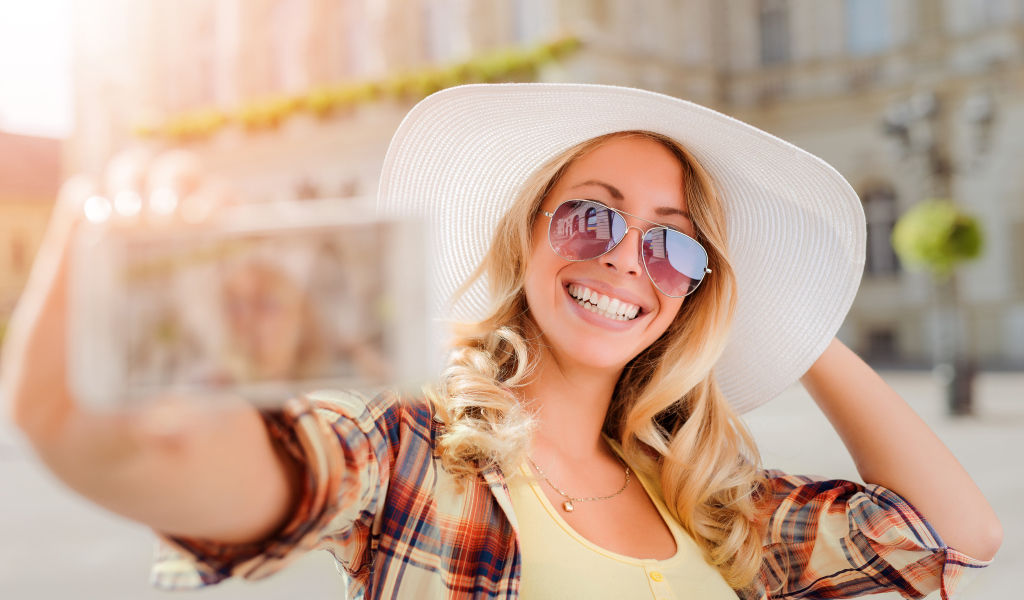 Улыбающаяся девушка в очках и большой белой шляпе 
