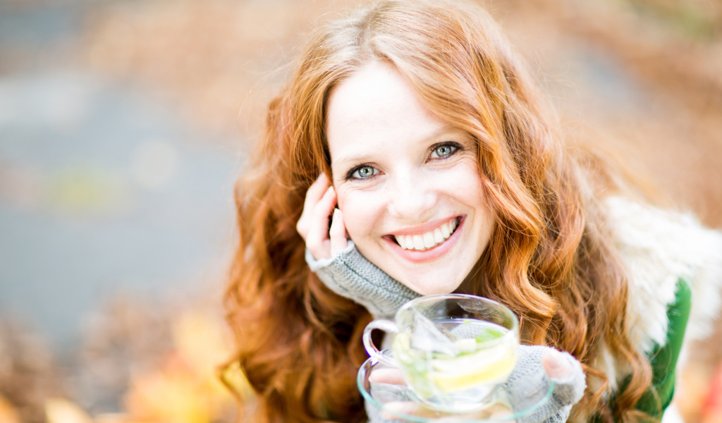 Улыбающаяся рыжеволосая девушка с чашкой чая в руке