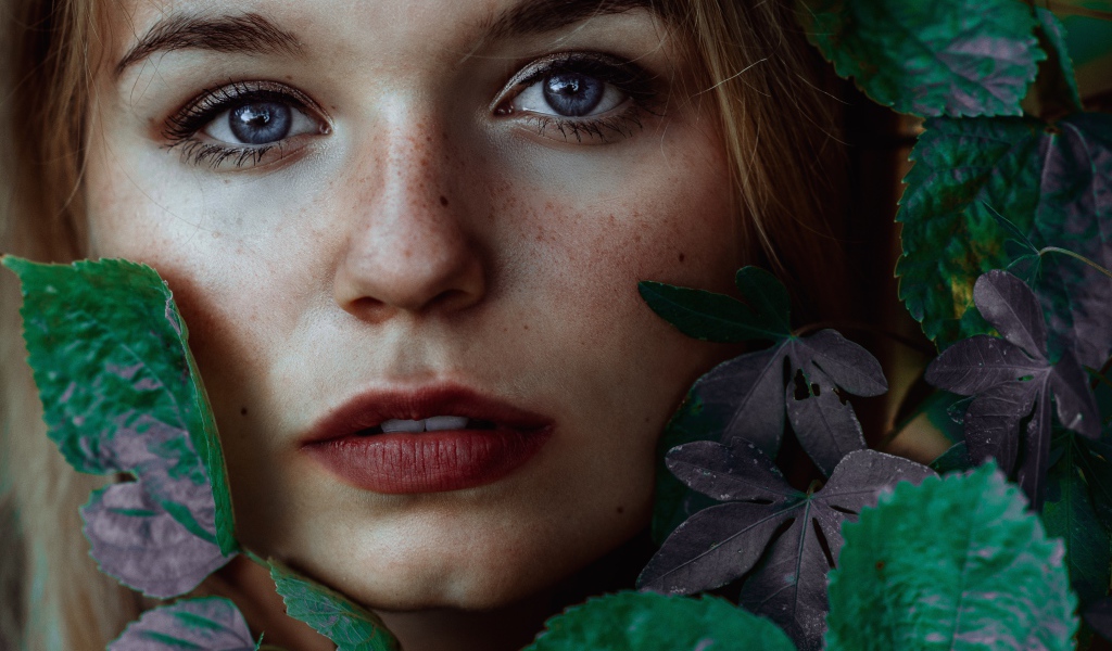 Лицо красивой голубоглазой девушки украшено зелеными листьями