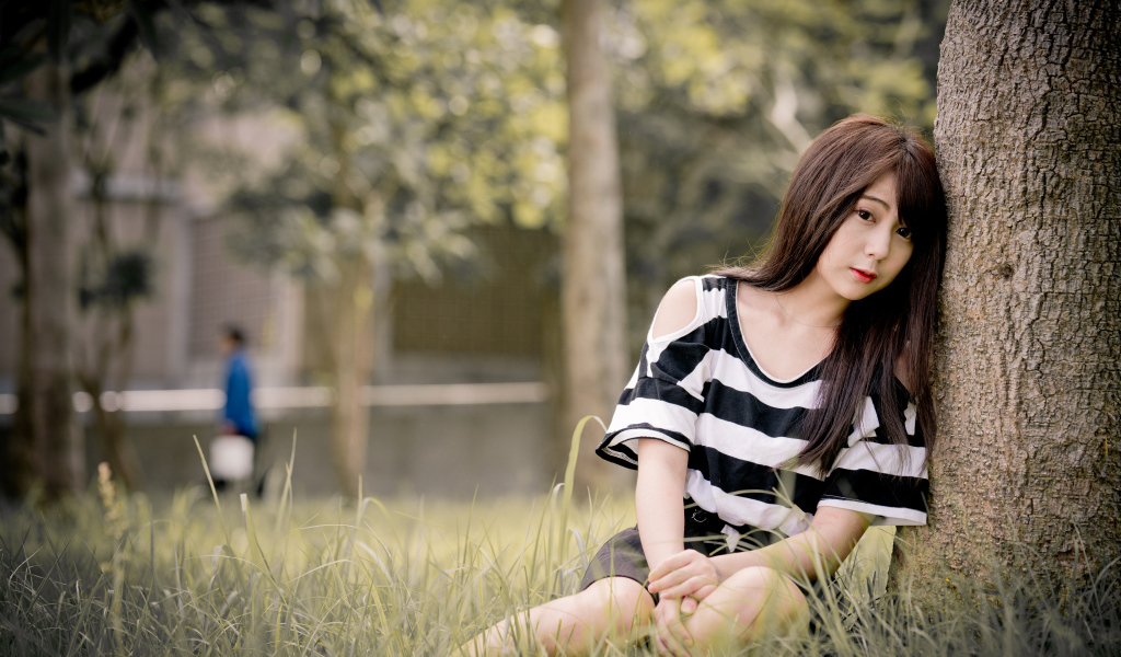 Молодая девушка азиатка сидит на траве у дерева