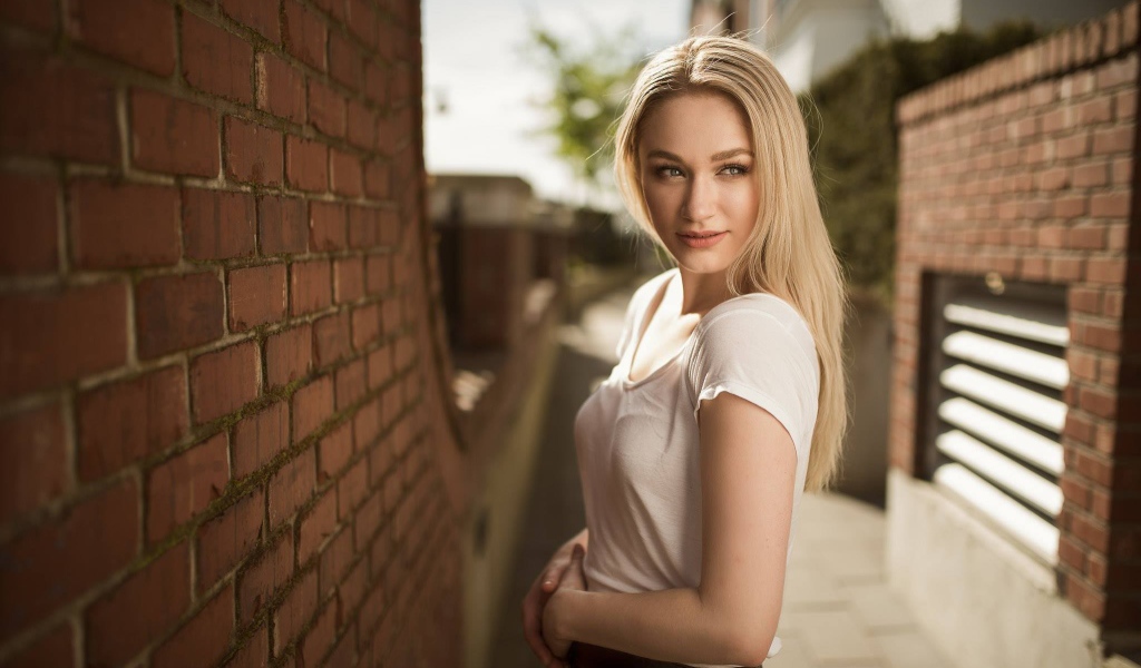 Молодая девушка блондинка у кирпичной стены 