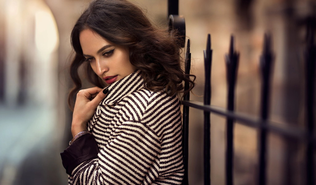 Молодая брюнетка в пальто у забора