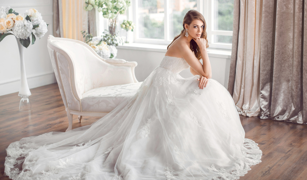 Молодая девушка в красивом свадебном платье сидит в белом кресле