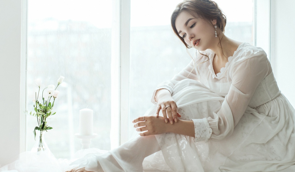 Молодая грустная девушка в белом платье у окна