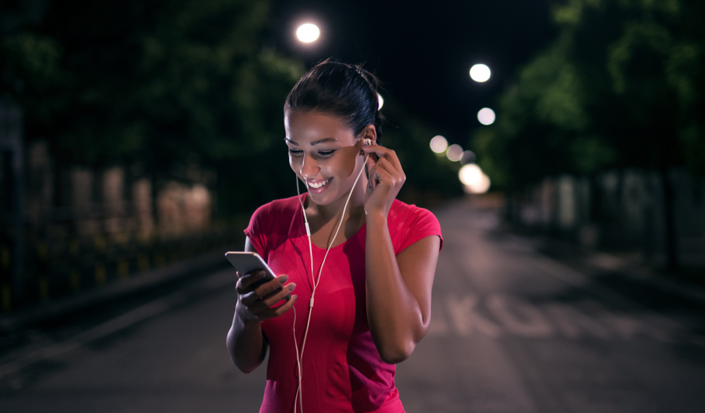 Молодая улыбающаяся девушка в наушниках с телефоном в руках