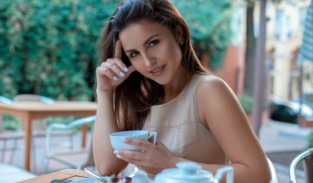 Молодая улыбающаяся девушка с чашкой кофе в кафе