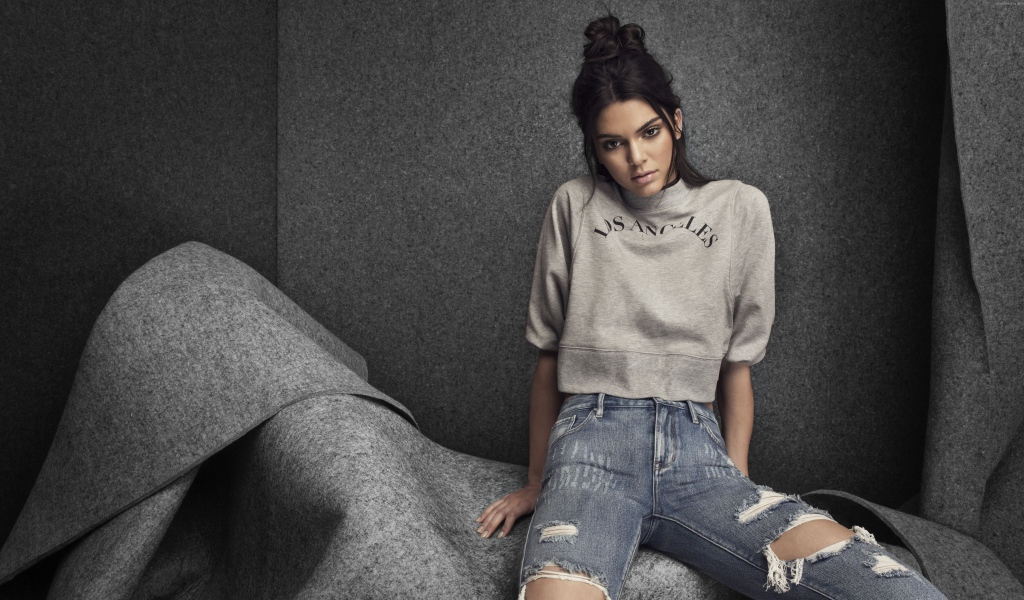 Модель Кендалл Дженнер в рваных джинсах на сером фоне
