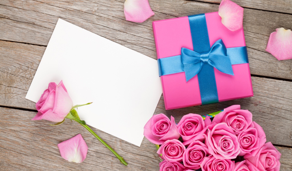 Box with a gift on the table with a bouquet of pink roses and a sheet of paper