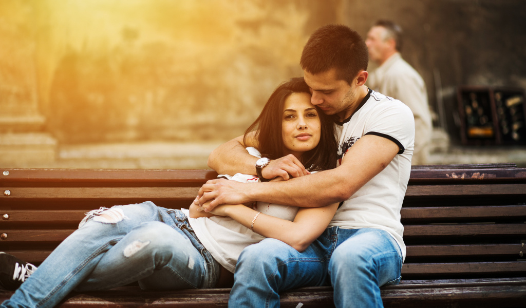 Влюбленная пара сидит на деревянной лавке в парке