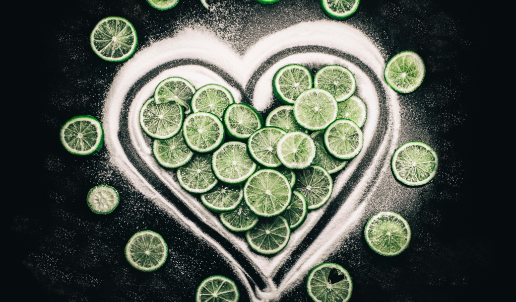 Сердце из сахара и кружочков  зеленого лайма на черном фоне