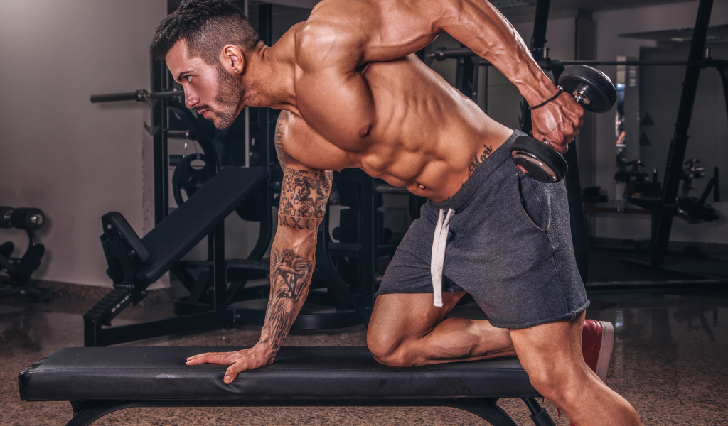 Мускулистый мужчина занимается в спортзале с гантелей