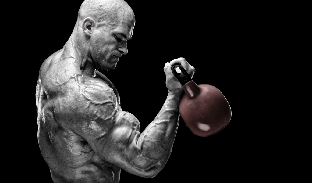 Сильный накаченный мужчина бодибилдер с гантелей в руках