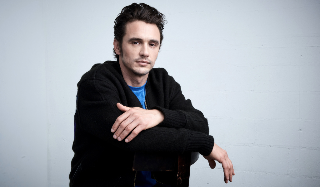 Актер Джеймс Франко в черной кофте на сером фоне